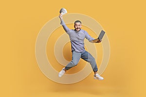 Online Lottery. Asian man with cash and laptop jumping on yellow background