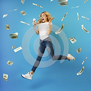Online Lottery. Overjoyed Woman Jumping With Smartphone Under Money Shower, Celebrating Victory