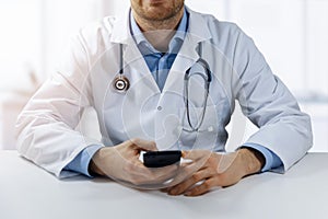 Online medical consultation - physician sitting by the table and using smart phone