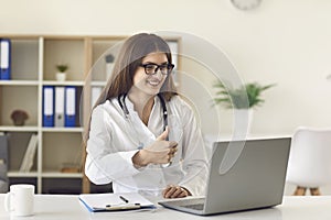 Online medical service. Female doctor showing thumb up gesture to patient on web. GP talking to client on laptop