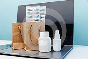 Online medical shopping concept. Paper bags with drugs and pills and conteiners on laptop on blue background