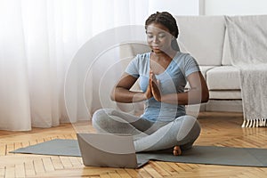 Online Meditation. Black Lady Practicing Yoga In Front Of Laptop At Home