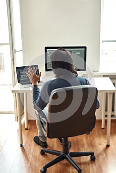 Online meeting with colleagues. Back view of male web developer looking at webcam and waving while sitting at his photo