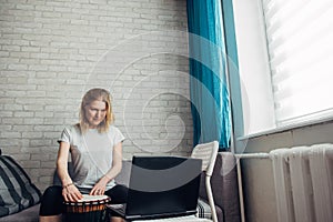 Online music lessons during quarantine due to coronavirus pandemic. Remote teaching to play the drum. Young woman watches video