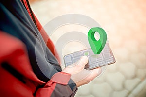 Online navigation, GPS and Geocaching. Green geolocation sign above the smartphone screen with an abstract online map. Close-up of