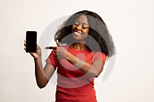 Online Offer. Cheerful Black Female Pointing On Blank Smartphone In Hand