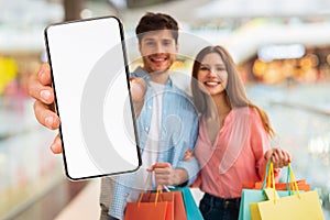 Online Offer. Young Couple Standing In Shopping Center And Showing Blank Smartphone