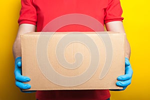 Online ordering and delivery. A man in a red uniform and rubber medical gloves holds a box on a bright yellow background. Food