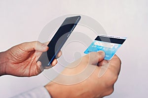 Online payment concept. Man using credit card with mobile phone at white background. Male hands holding smartphone with blank