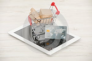 Online payment concept. Small shopping cart with bank card, boxes and tablet on white table