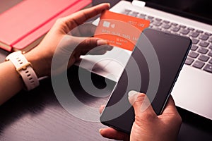 Online payment concept. Woman`s hands holding a credit card and using smart phone for online shopping on the laptop