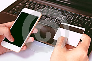 Online payment, man's hands holding a credit card over laptop and using smart phone for online shopping on the desk in the of