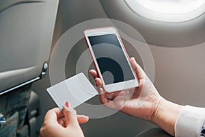 Online payment, Woman`s hands holding a credit card and using smart phone for online shopping in the plane