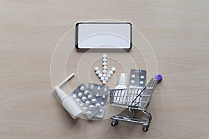 Online pharmacy concept with home delivery. Buying medicine online by phone. Mini trolley with different tablets, sprays