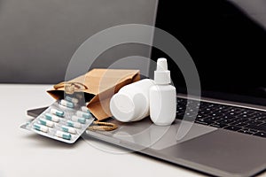 Online pharmacy concept. Pills and spray white mockup containers and buff paper bags over the laptop