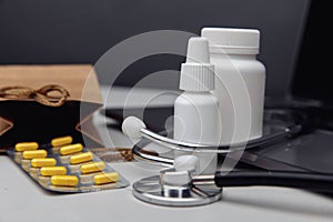 Online pharmacy concept. Pills, stethoscope and spray containers and buff paper bags on the laptop