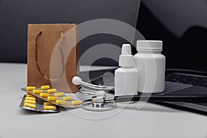 Online pharmacy concept. Pills, stethoscope and spray containers and buff paper bags near the laptop