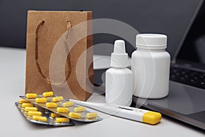 Online pharmacy concept. Pills, thermometer and spray containers and buff paper bags on the laptop close-up