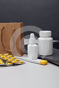 Online pharmacy concept. Pills, thermometer and spray containers and buff paper bags on the laptop close-up. Vertical