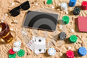 Online poker game on the beach with digital tablet and stacks of chips. Top view