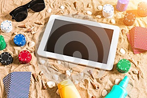 Online poker game on the beach with digital tablet and stacks of chips. Top view