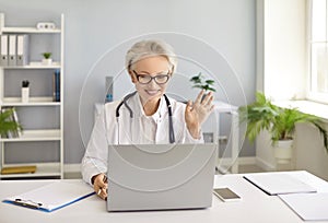 Online practitioner video calling her patient and waving hello at laptop computer
