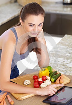 An online recipe could be good.... An attractive young woman looking for recipes on her digital tablet while cooking.