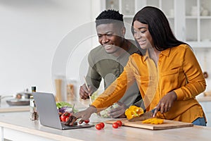 Online Recipe. Joyful black couple using laptop computer in kitchen while cooking
