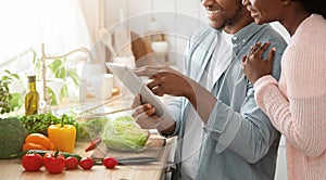 Online Recipe. Smiling black couple using digital tablet in kitchen, cooking together