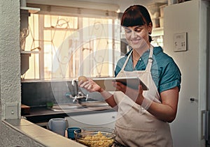 Online recipes are always the best. an attractive young woman following an online recipe on her digital tablet while