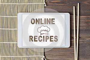 Online recipes. Cookbook in a tablet computer. Chopsticks and a bamboo tablecloth.Brown wooden background