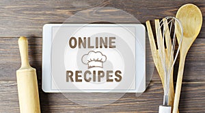 Online recipes. Cookbook in a tablet computer. Kitchen utensils. Brown wooden background