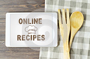 Online recipes. Cookbook in a tablet computer. Kitchen utensils. Brown wooden background