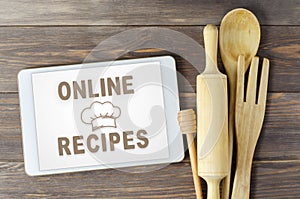 Online recipes. Cookbook in a tablet computer. Kitchen utensils. Brown wooden background