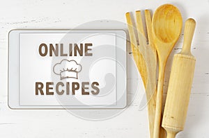 Online recipes. Cookbook in a tablet computer. Kitchen utensils. White wooden background