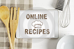 Online recipes. Cookbook in a tablet computer. Kitchen utensils. White wooden background