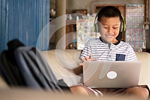 Online remote learning, distance education and homeschooling concepts. School kid Asian preteen boy in headphone using laptop