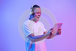 Online Sales. Excited Black Man In Wireless Headphones Holding Digital Tablet