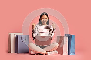 Online Sales. Overjoyed Asian Woman With Laptop Sitting Among Bright Shopping Bags