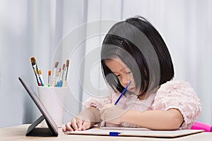 Online school concept. Asian cute girl painting on paper with watercolor paints. Child looking at touchpad.