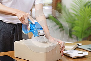Online selling concept, Asian business women packing product into parcel box and sealing with tape