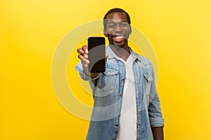 Online service, technology. Portrait of satisfied glad young man in denim casual shirt holding out cellphone. isolated on yellow