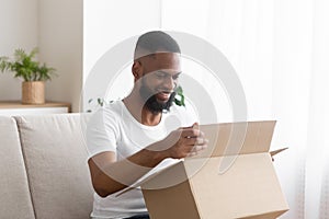 Online shopaholic. Glad african american man unpack parcel