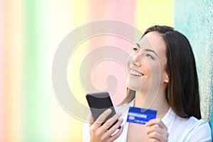 Online shopper thinking holding phone and credit card