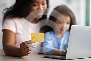 Online shopping. African American mother holding credit card, making purchases on web with her daughter, using laptop