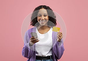 Online shopping app. Smiling young African American woman using cellphone and credit card, purchasing in web store