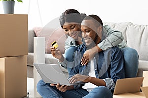 Online Shopping. Cheerful Black Spouses With Laptop Choosing Furniture After Moving Home