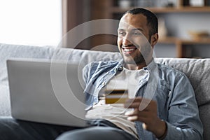 Online Shopping. Cheerful Handsome Black Man Using Laptop And Credit Card
