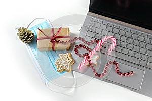 Online shopping for Christmas during coronavirus  pandemic, laptop with protective face mask, gift, sweets and holiday decoration