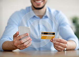 Online shopping. Closeup of Arab guy holding credit card and cellphone, making e-payment, ordering products on internet